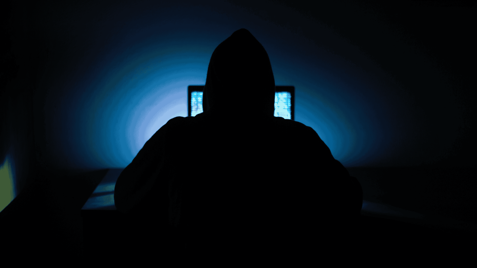Een figuur met capuchon in het donker, als beeld bij cybercriminaliteit