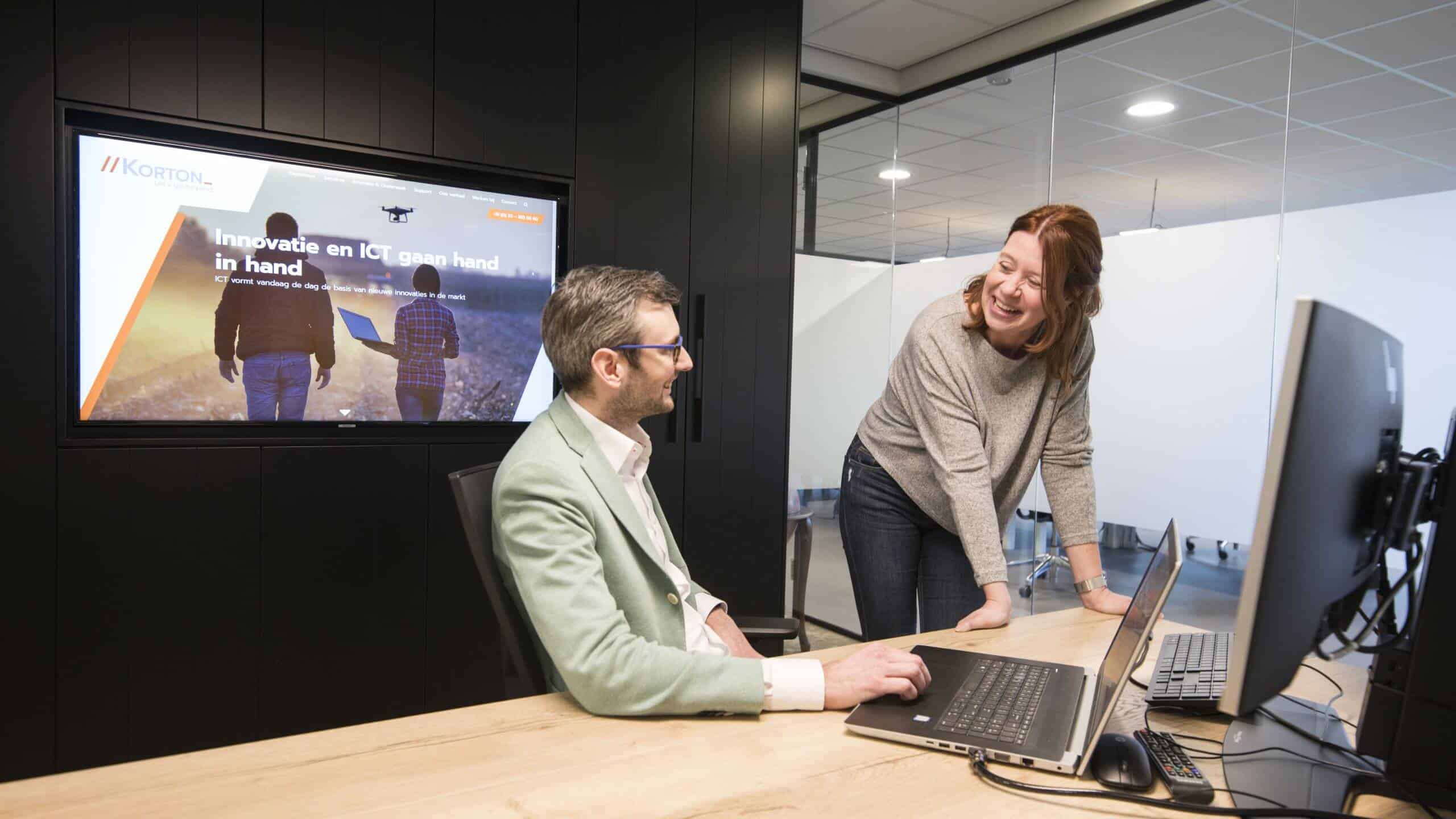 Twee collega's kijken samen naar een scherm in een vergaderruimte