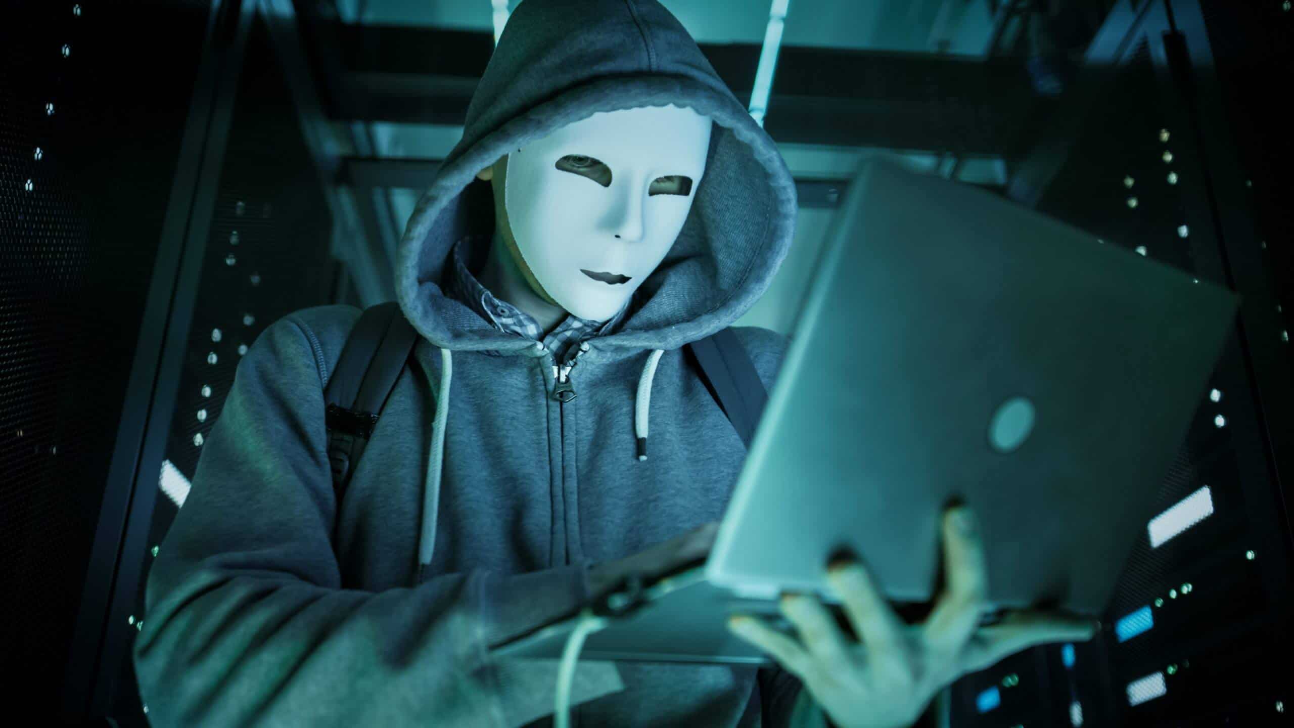Een figuur met capuchon achter een laptop, als beeld bij cybercriminaliteit