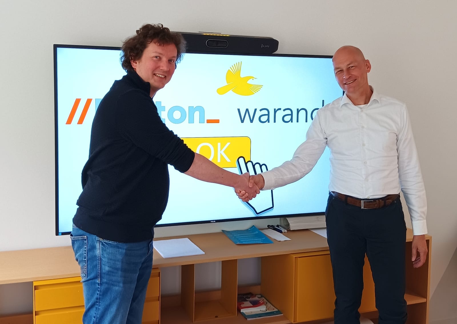 Twee mensen geven elkaar een hand voor het scherm met de logo's van Korton en Warande